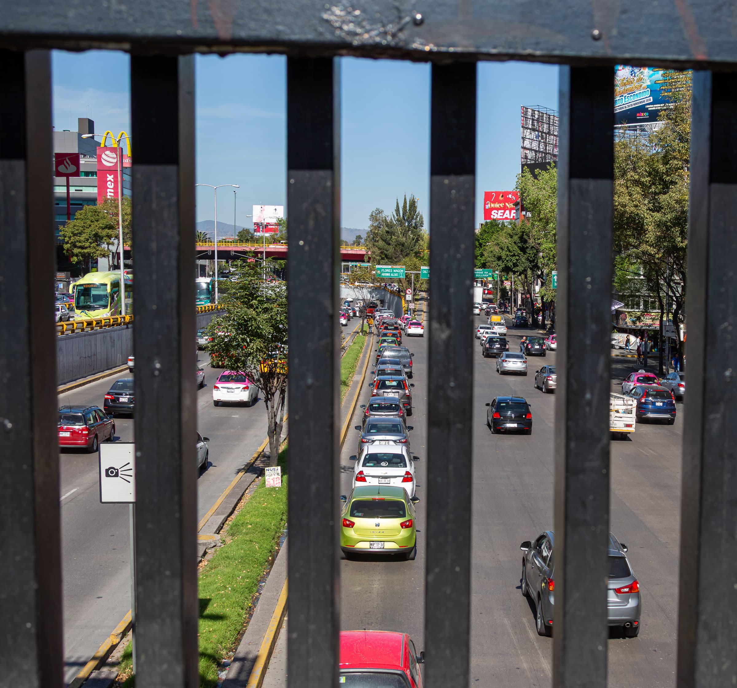 A line of cars in Mexico City aligned within a narrow opening of a foreground railing in Between the Bars by Francisco Colón.