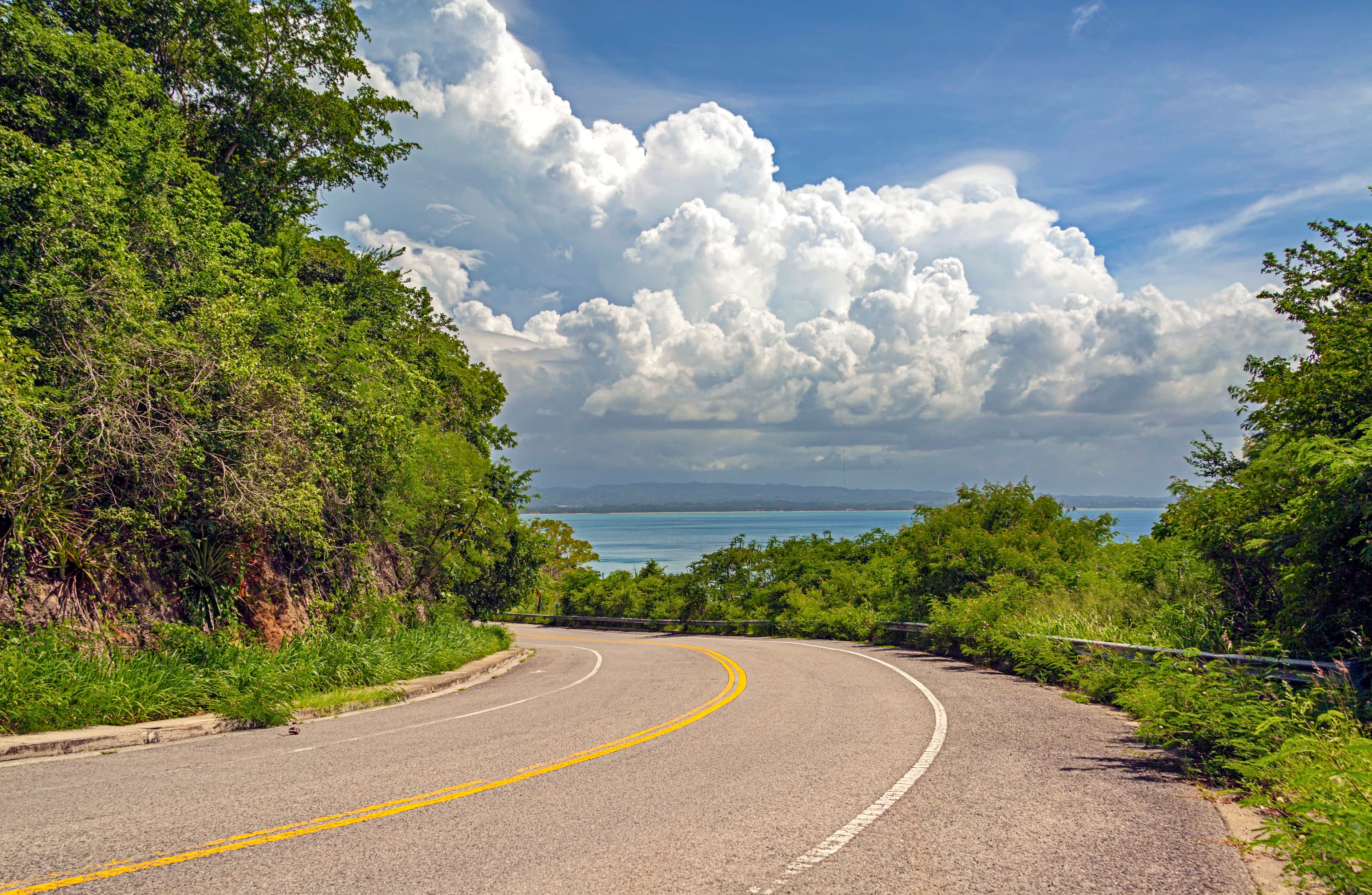 Curving road descending toward the Atlantic coast beneath dramatic clouds in Puerto Rico, titled Journey to the Horizon by Francisco Colón.