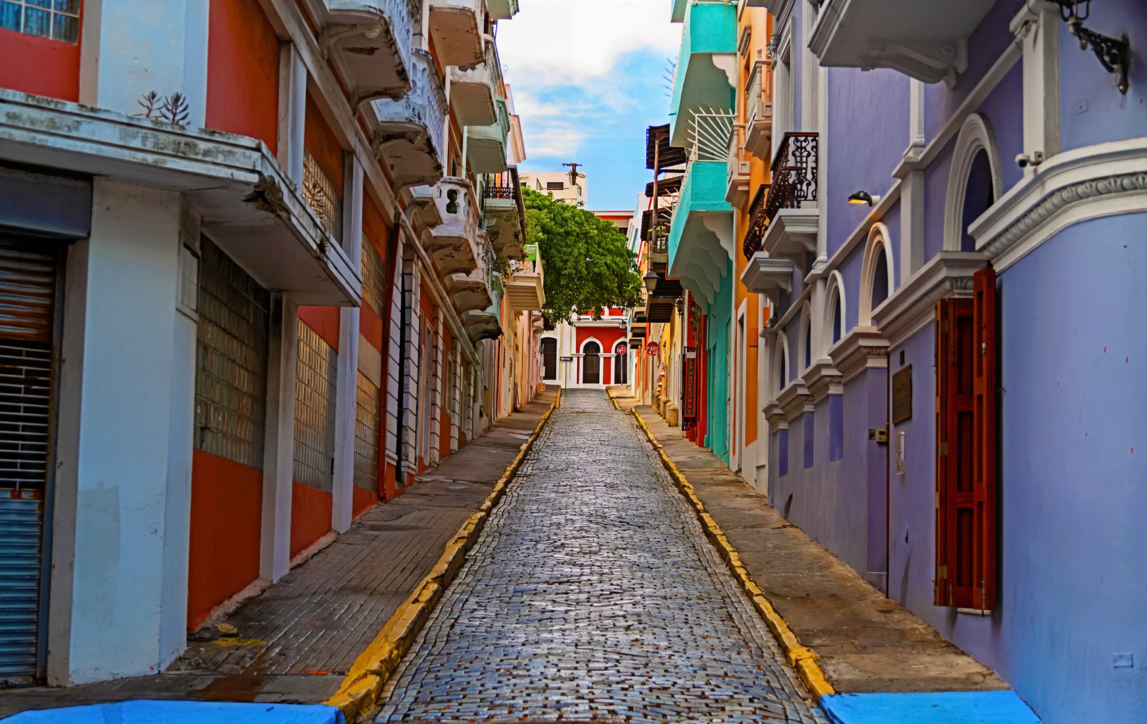 Empty cobblestone street rising between colorful historic buildings in Old San Juan, Puerto Rico, titled The Road to Discovery by Francisco Colón.