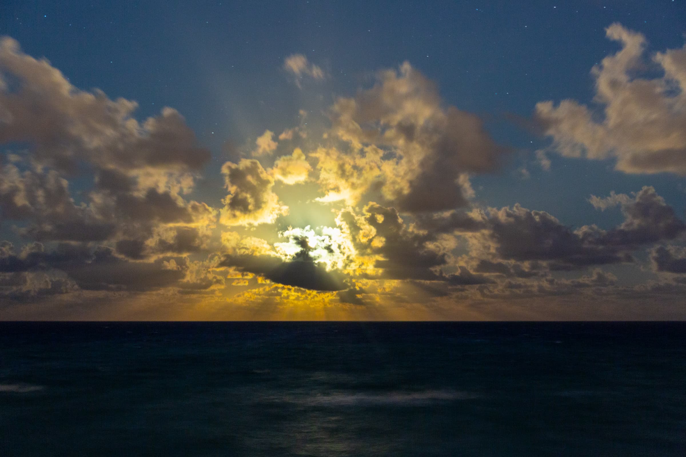 Sunrise breaking through dramatic clouds above the Atlantic Ocean at Lake Worth Beach, with faint stars still visible in the morning sky.