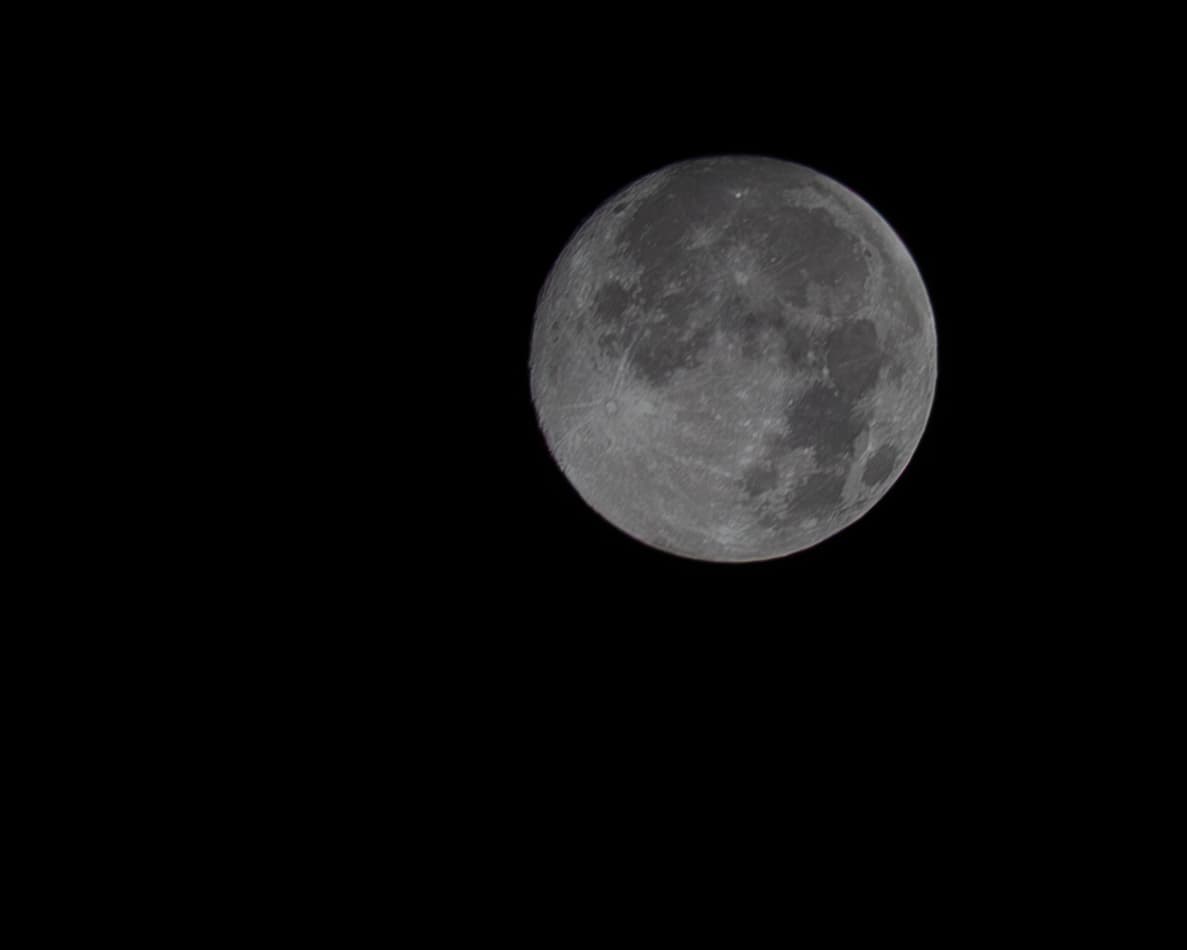 A nearly full Moon appears in the upper-right portion of a deep black sky, surrounded by expansive negative space in a minimalist handheld photograph made in Mexico.