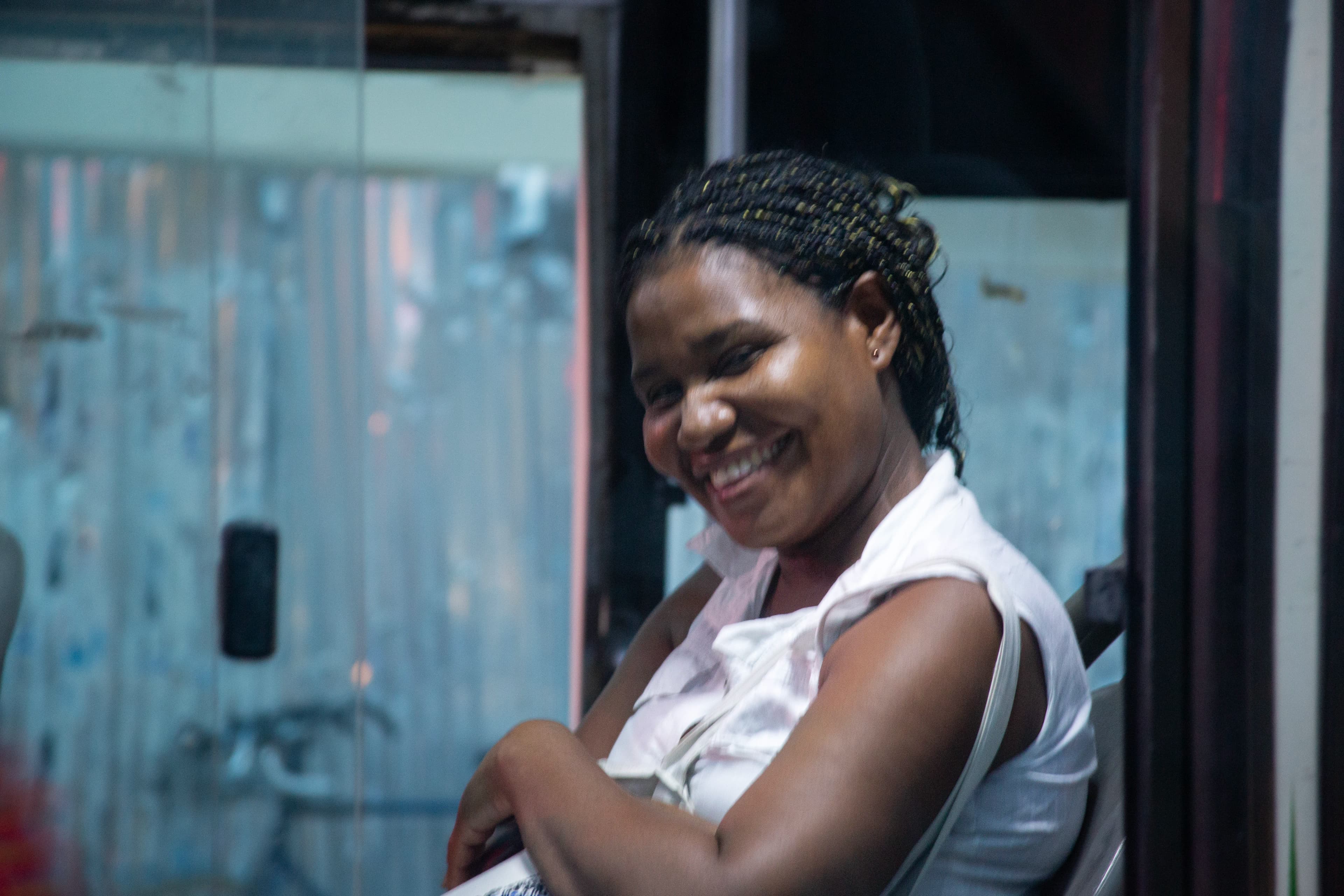 A smiling woman seated inside a bus in Cartagena looks toward the photographer through the windows separating their two vehicles.