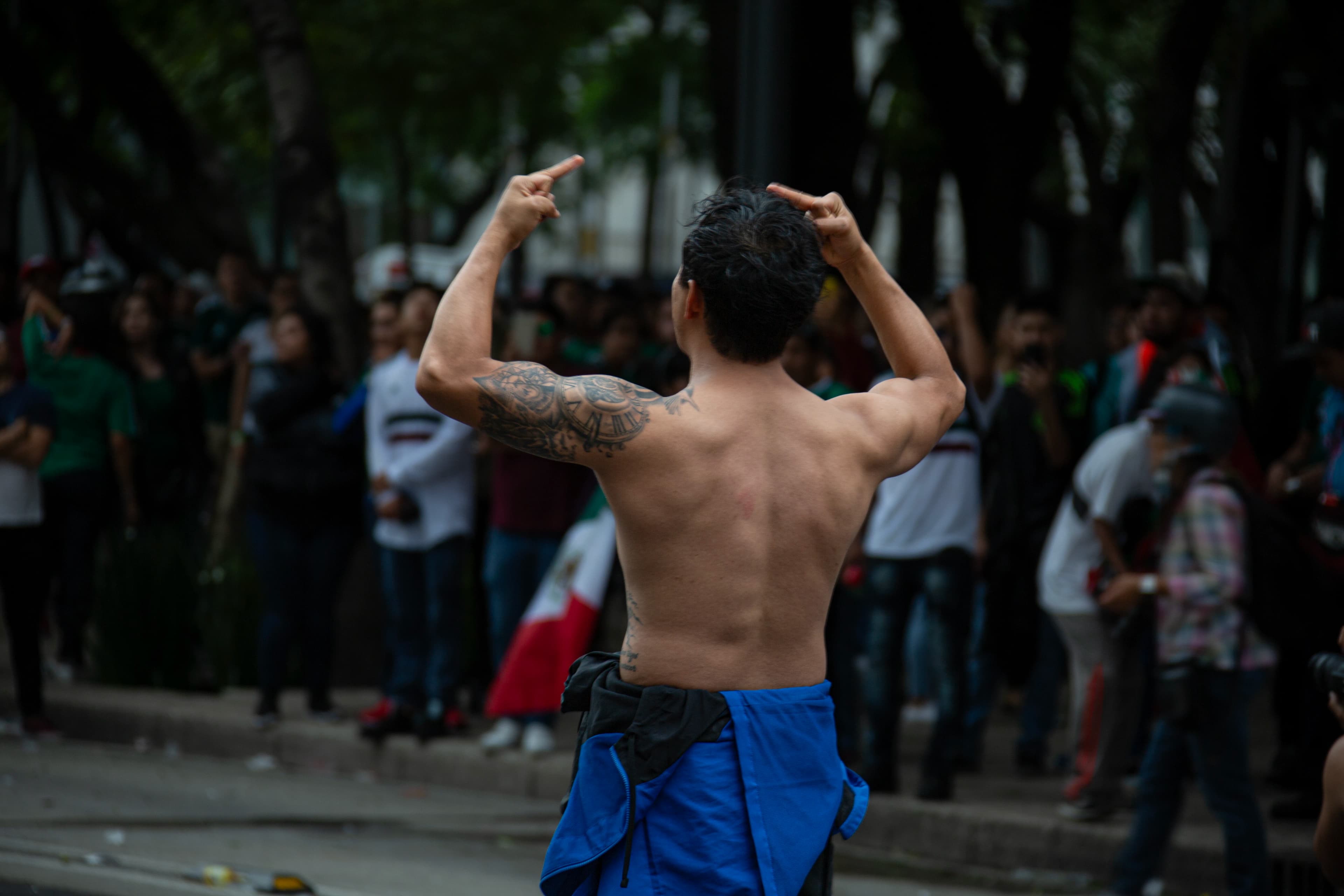 An unidentified shirtless demonstrator photographed from behind raises both middle fingers during an animal-rights protest in Mexico City as a crowd gathers in the softly focused background.