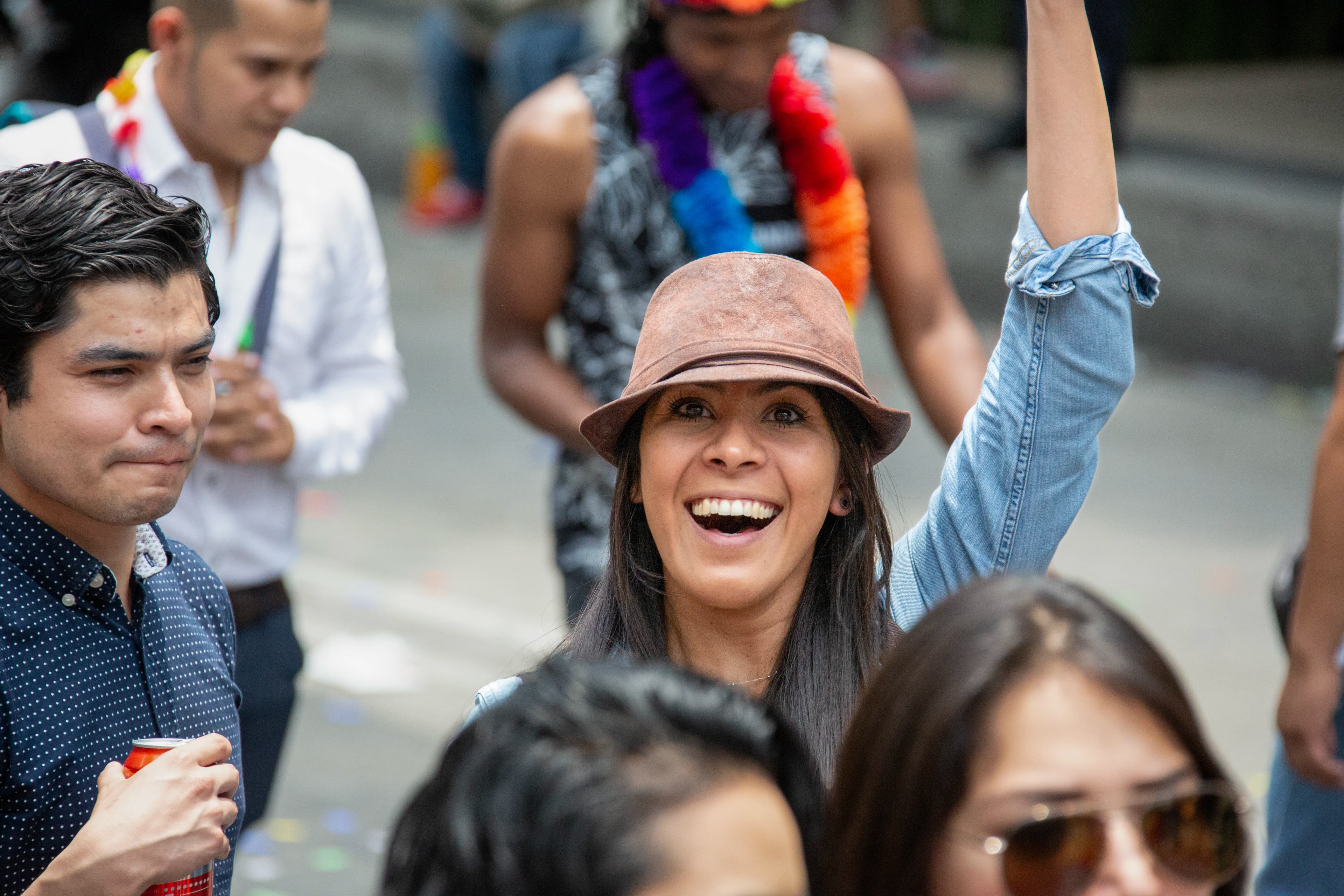 A smiling woman at Mexico City Pride looks directly toward the photographer with one arm raised, surrounded by participants in a crowded street celebration.