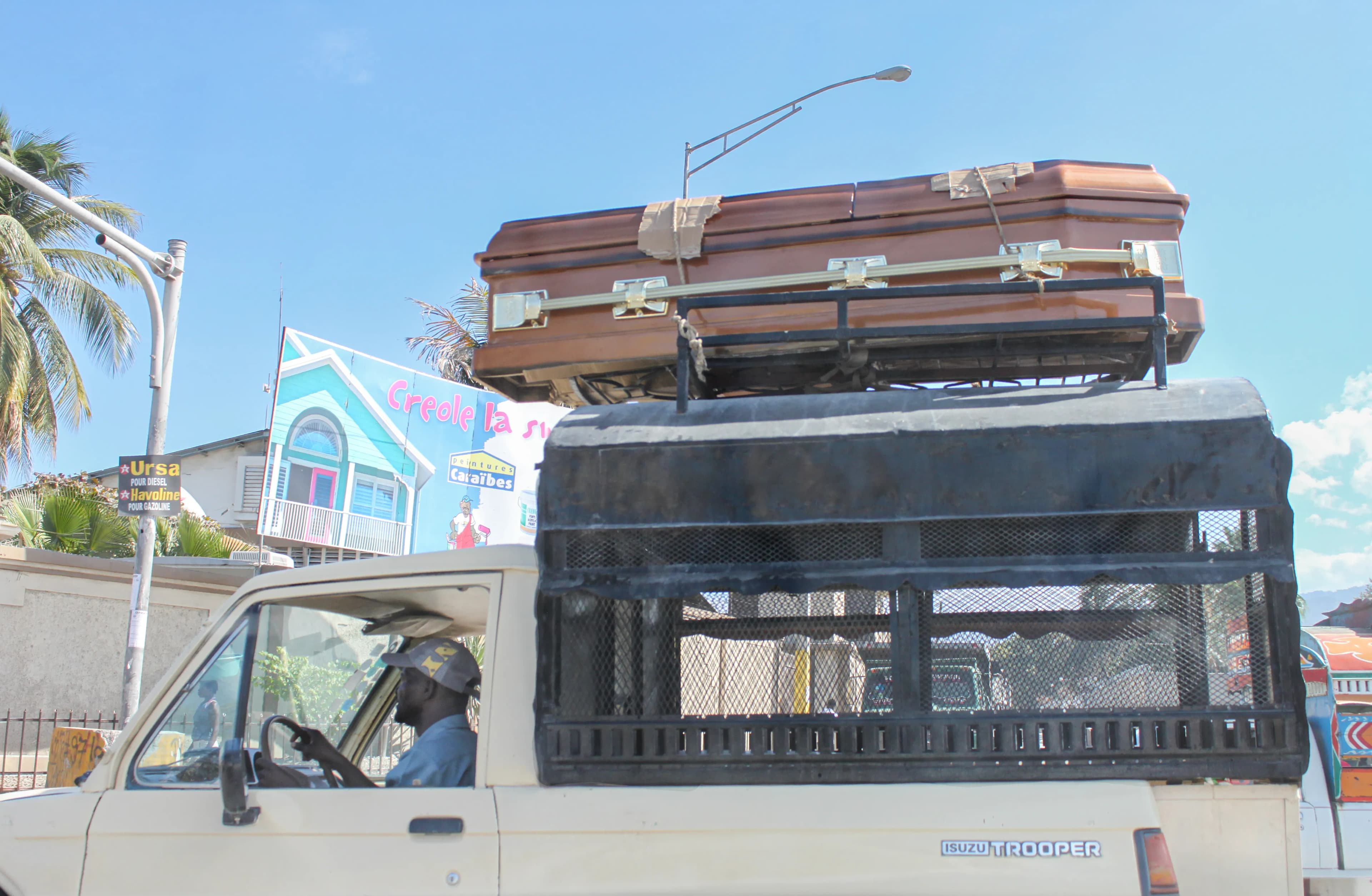 Driver traveling through Port-au-Prince, Haiti, with a coffin secured above his vehicle on January 14, 2012, titled The Passenger Above by Francisco Colón.