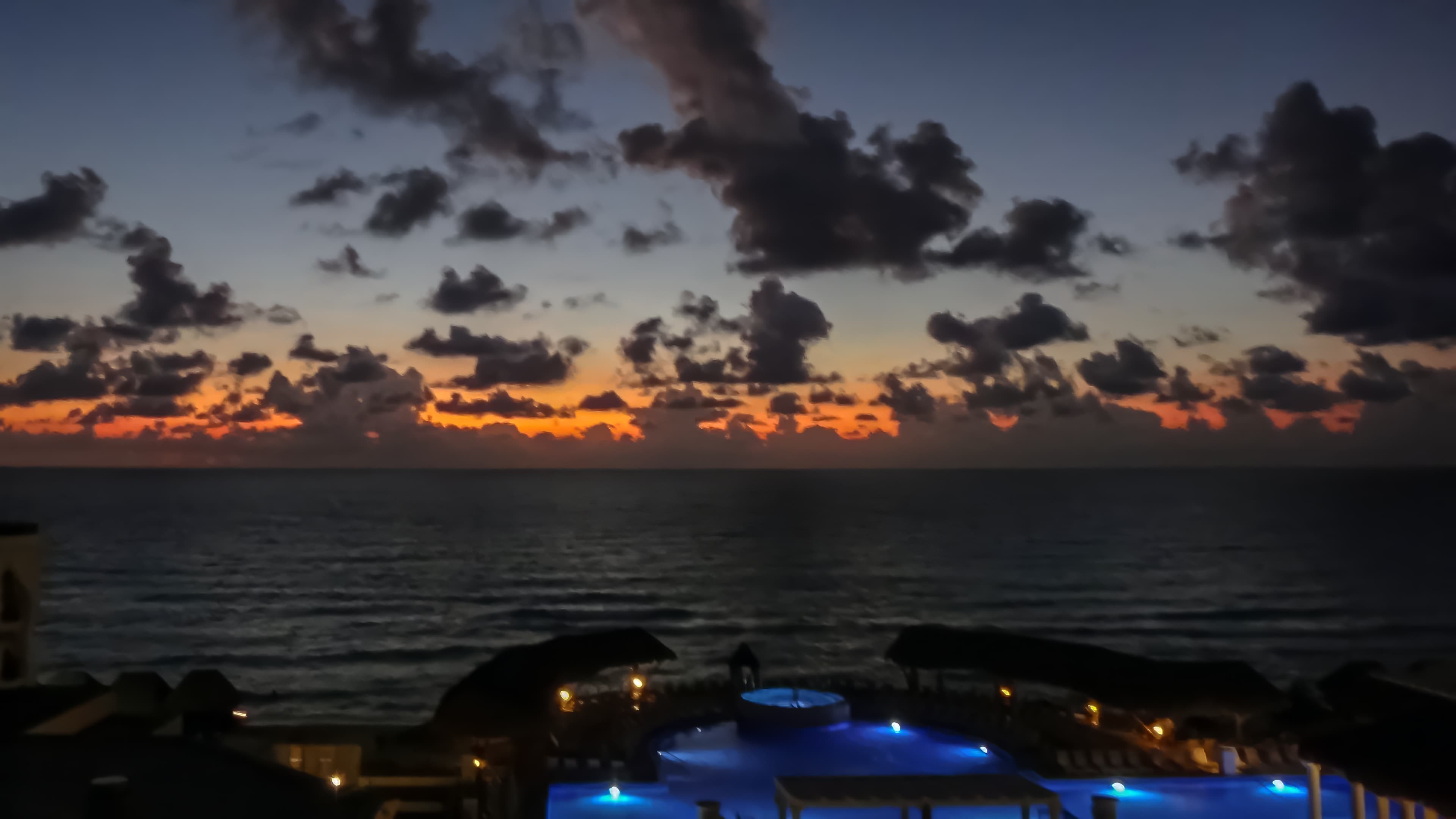 Caribbean sunrise above the ocean and an illuminated blue pool at the Marriott Cancún, titled Misma llave, misma puerta by Francisco Colón.