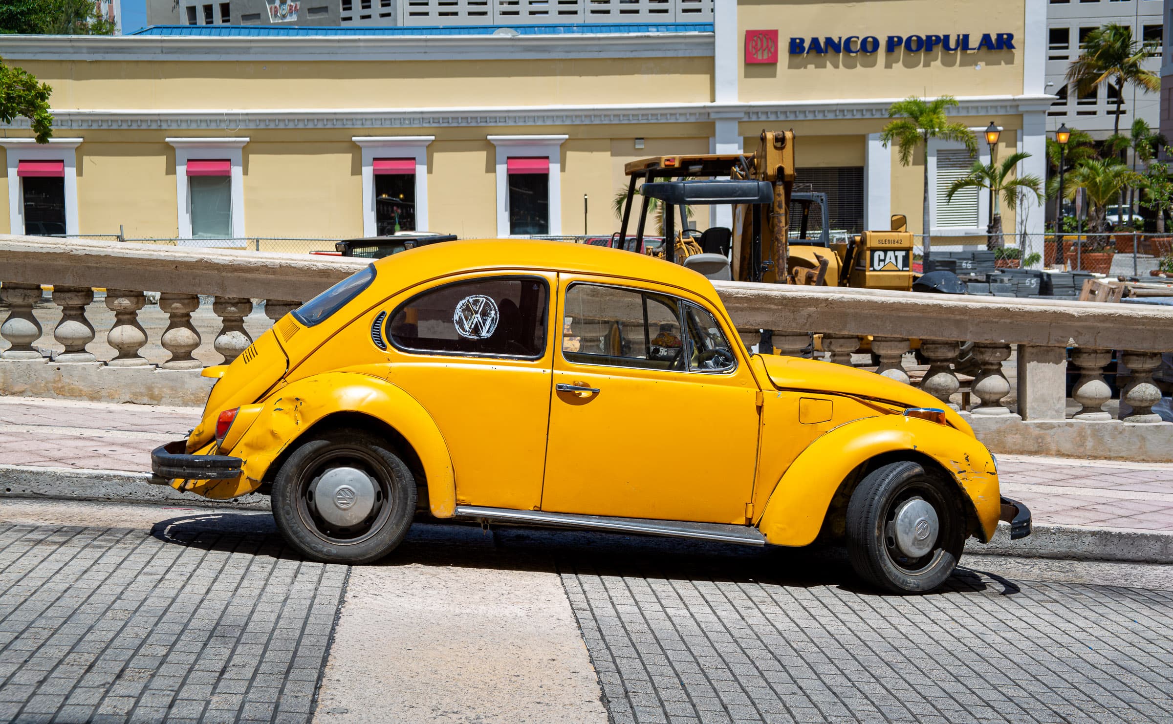 A weathered yellow Volkswagen Beetle parked along a street in Old San Juan, Puerto Rico, in The Car That Takes Me Back by Francisco Colón.