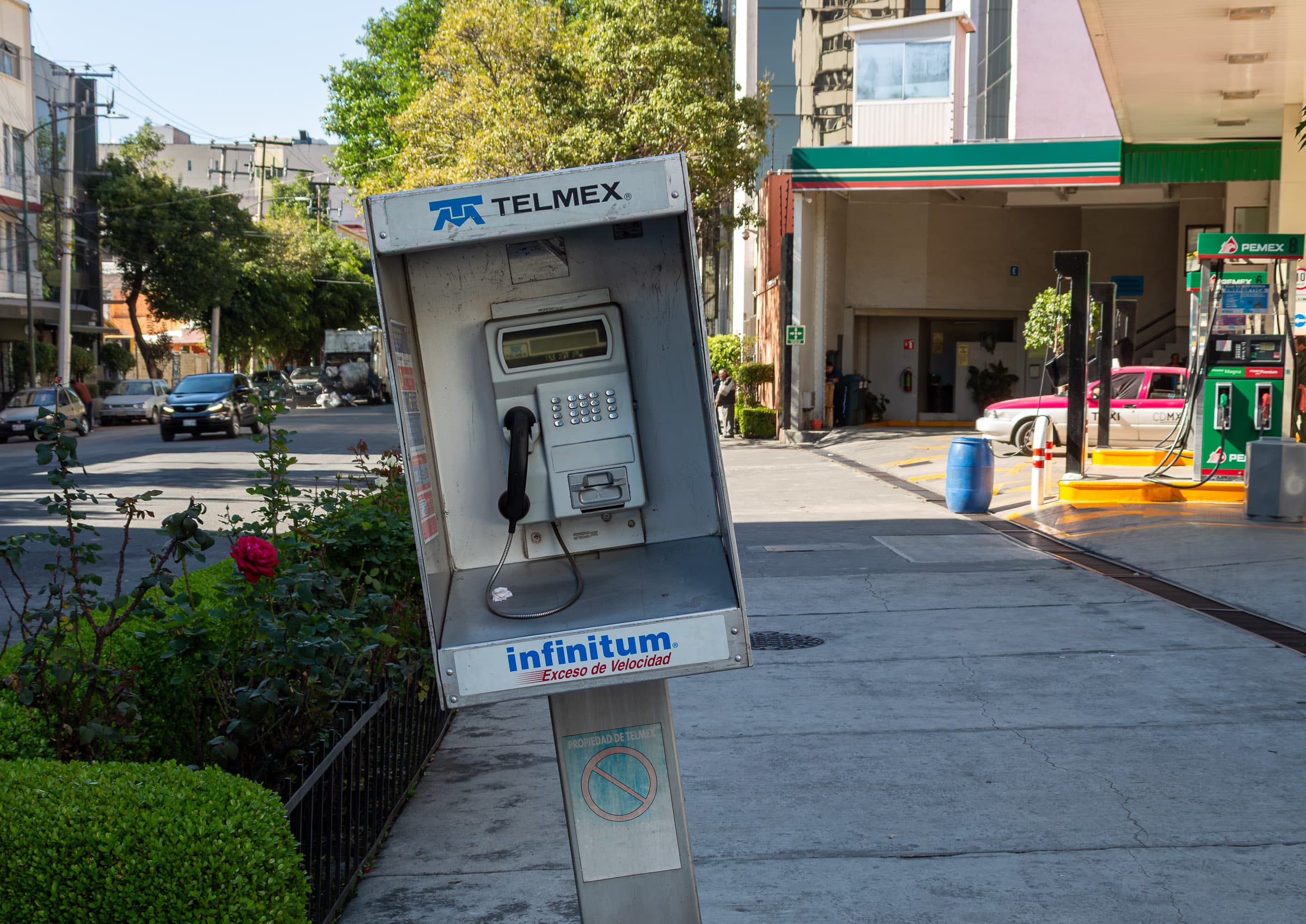 A heavily leaning Telmex public telephone with an Infinitum Internet advertisement along a street in Mexico City, photographed by Francisco Colón.