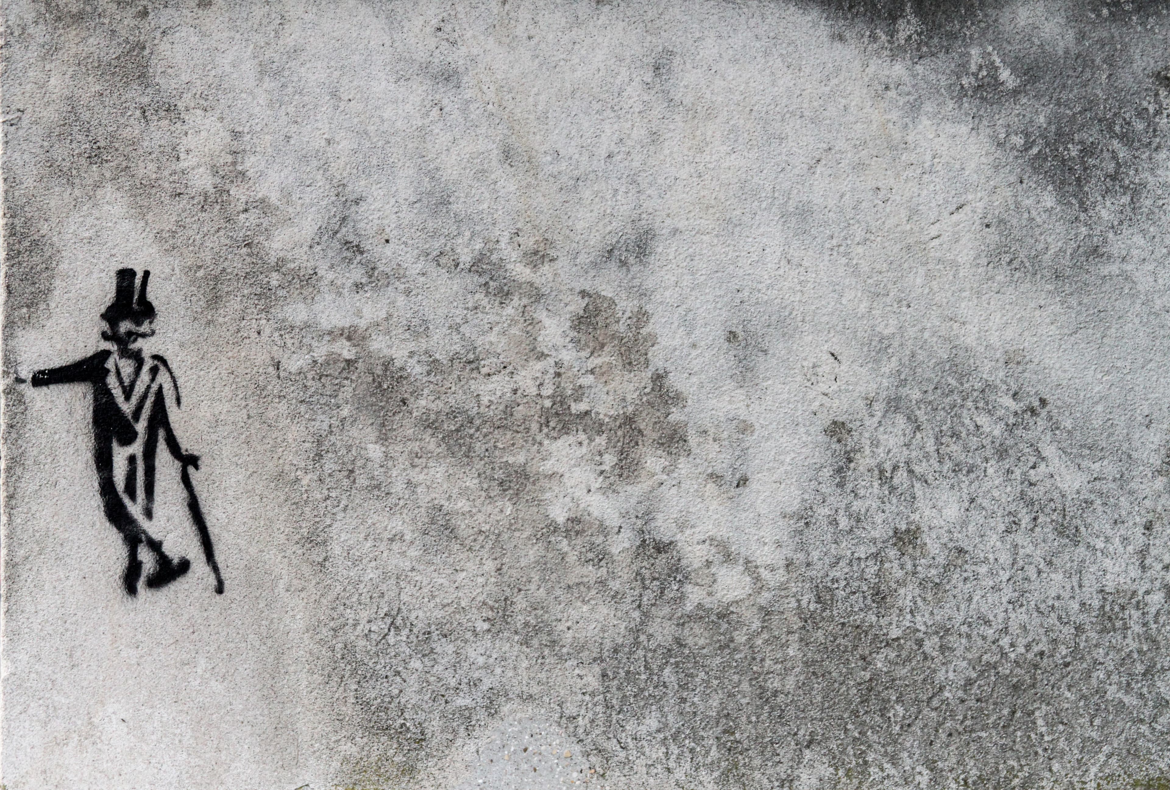 A small black stencil of a gentleman wearing a top hat and carrying a cane steadies himself against an expansive weathered wall near the Musée de Cluny in Paris.