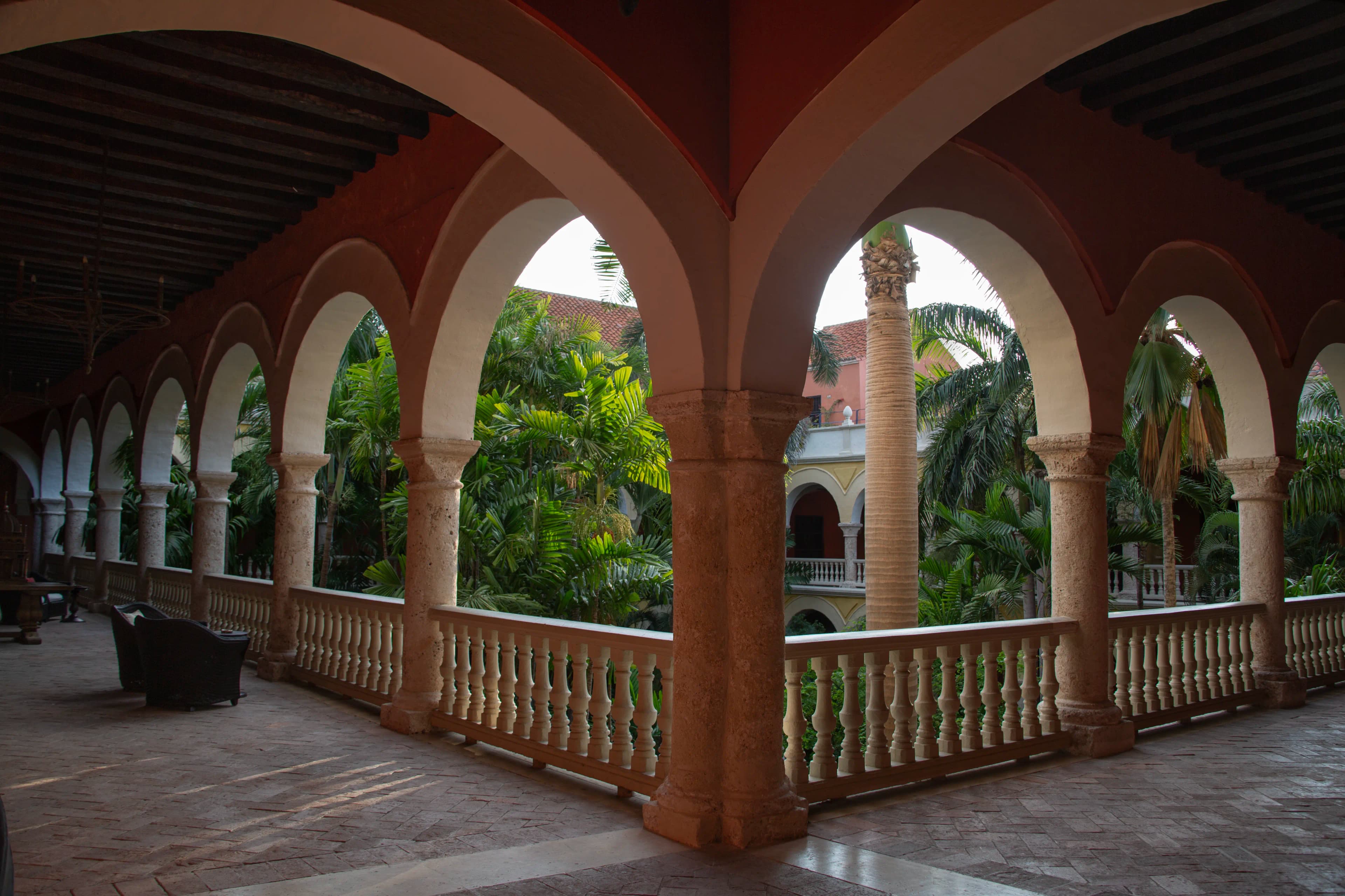 Repeating arches and a central stone column frame a tropical courtyard filled with palms inside a hotel in Cartagena, Colombia.