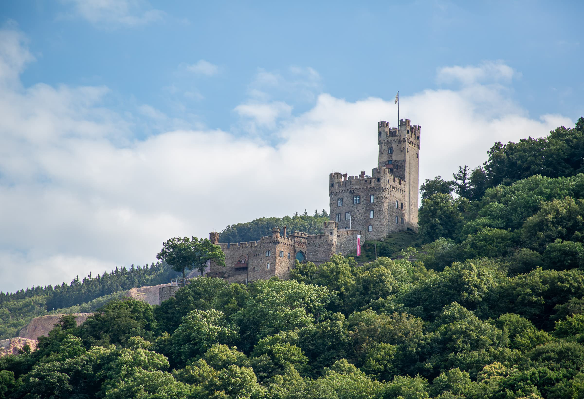 Sooneck Castle rises above a densely wooded hillside beneath a blue and cloud-filled sky along the Rhine River near Niederheimbach, Germany, in Along the Rhine, Together by Francisco Colón.