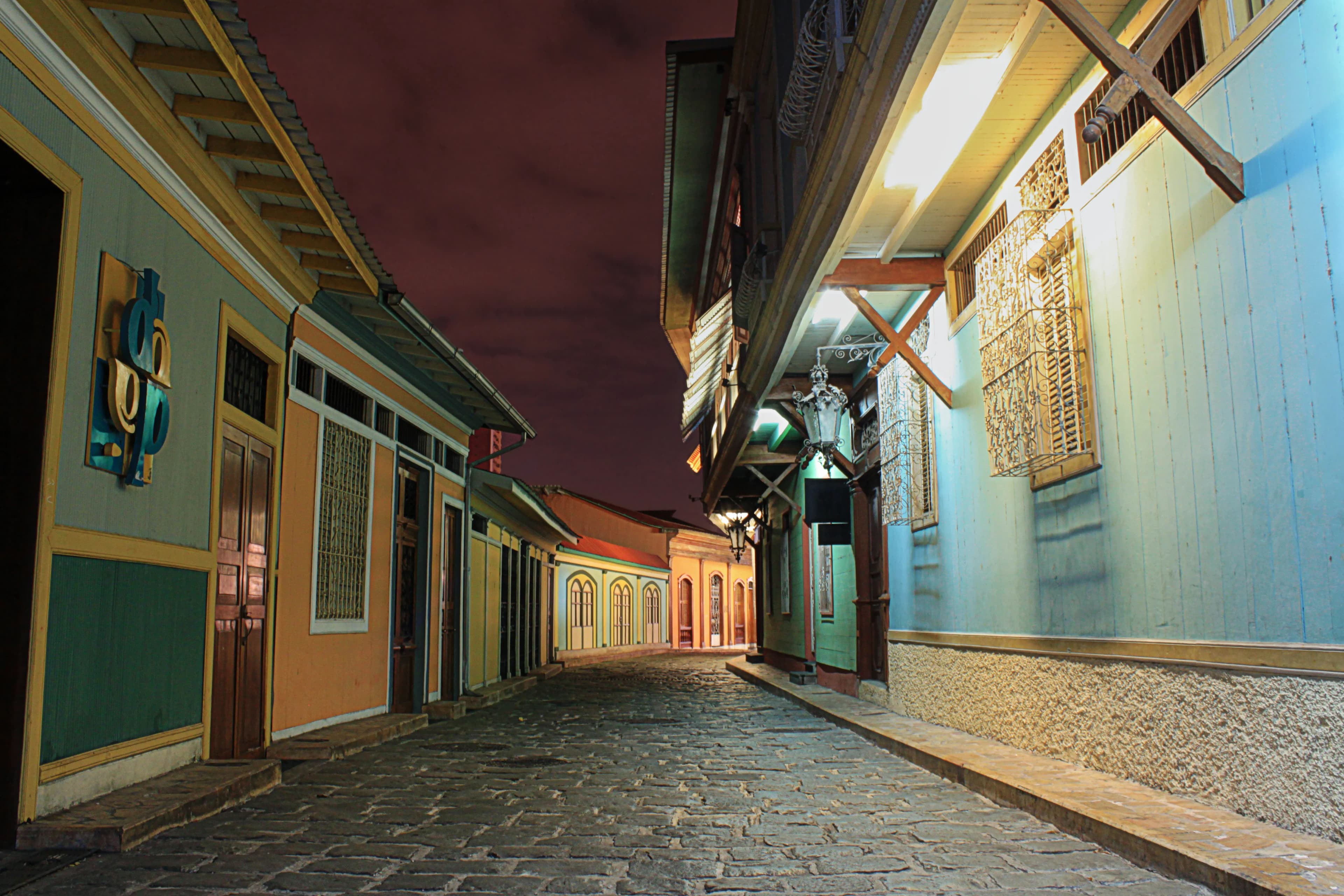 Cobblestone street at night between colorful historic buildings in Guayaquil, Ecuador, bending out of sight in the distance, titled Around the Corner by Francisco Colón.