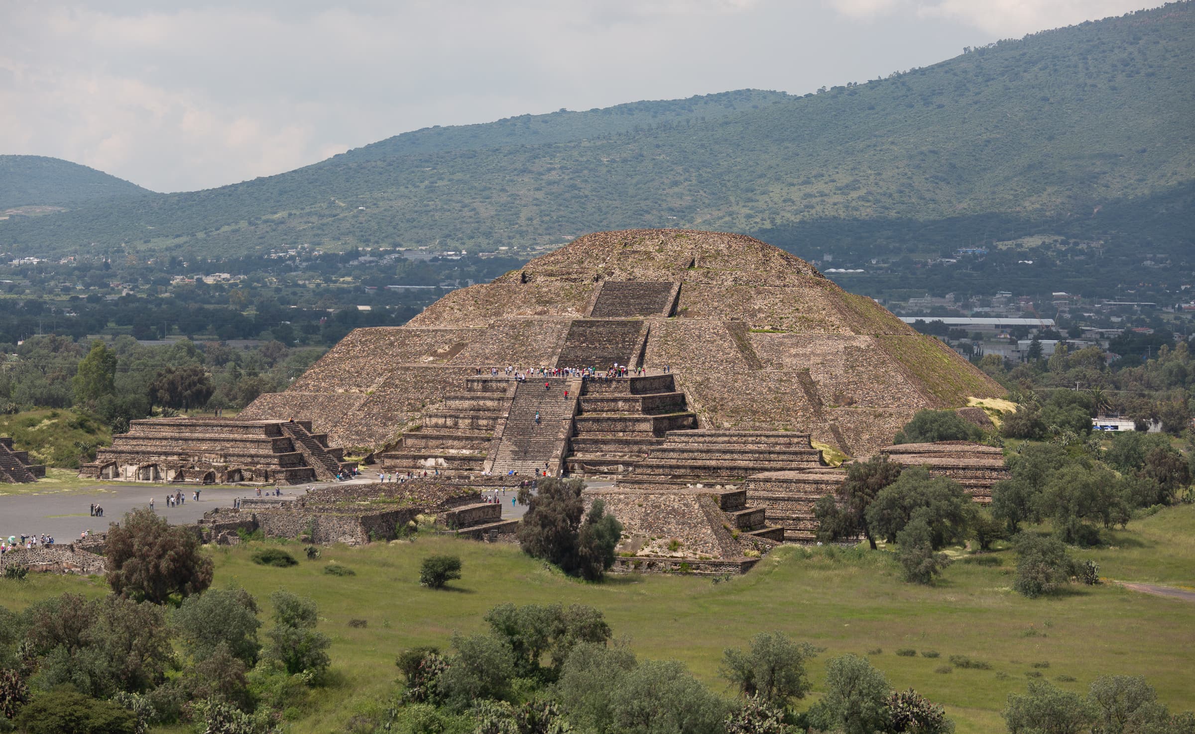 The Pyramid of the Moon at Teotihuacán rises before Cerro Gordo, with visitors visible along its central staircase and terraces.