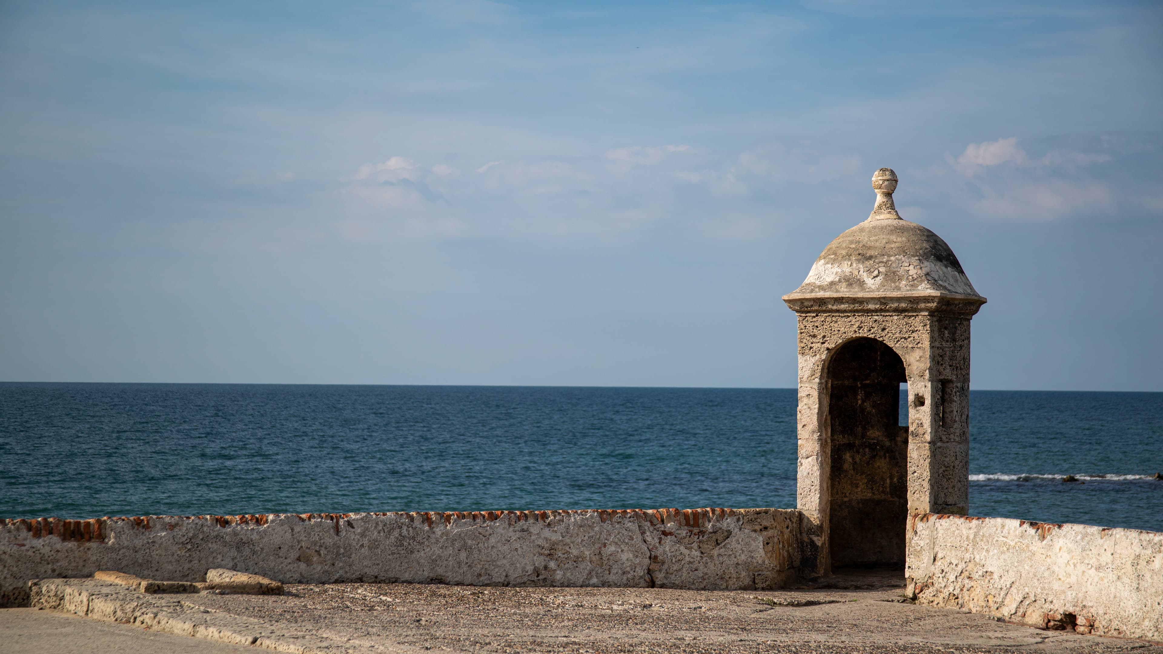 A weathered stone sentry post stands on Cartagena's historic fortified wall facing the Caribbean Sea beneath an open blue sky.