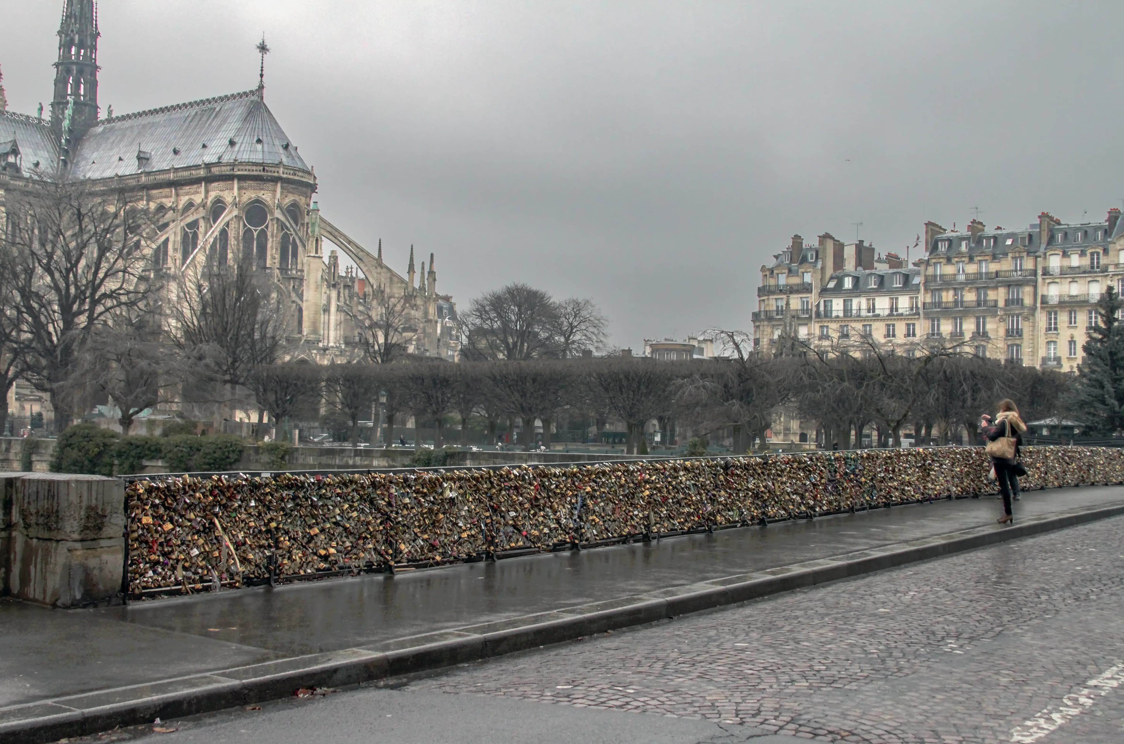 Thousands of love locks cover the Pont de l’Archevêché beside Notre-Dame as a woman photographs the bridge on a rainy day in Paris.