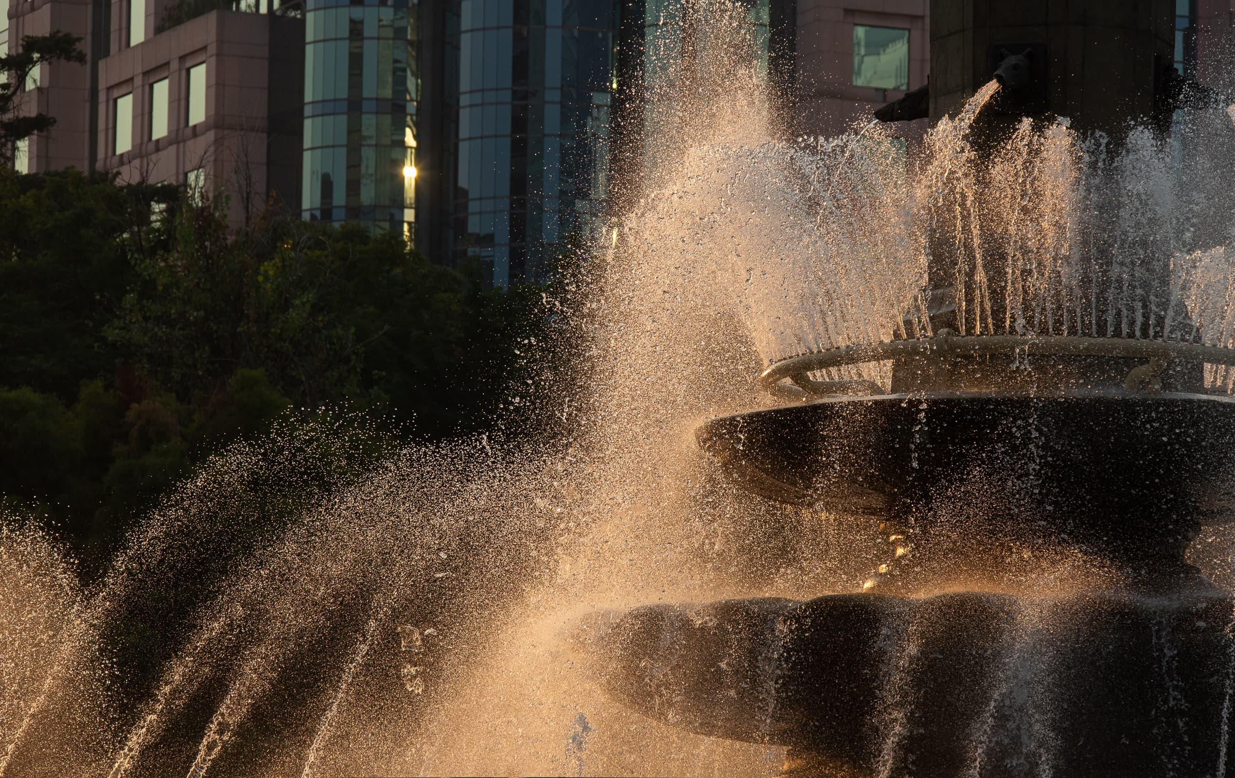 Backlit water droplets glowing around the dark tiers of La Diana fountain in Mexico City, photographed close enough that the statue remains outside the frame.