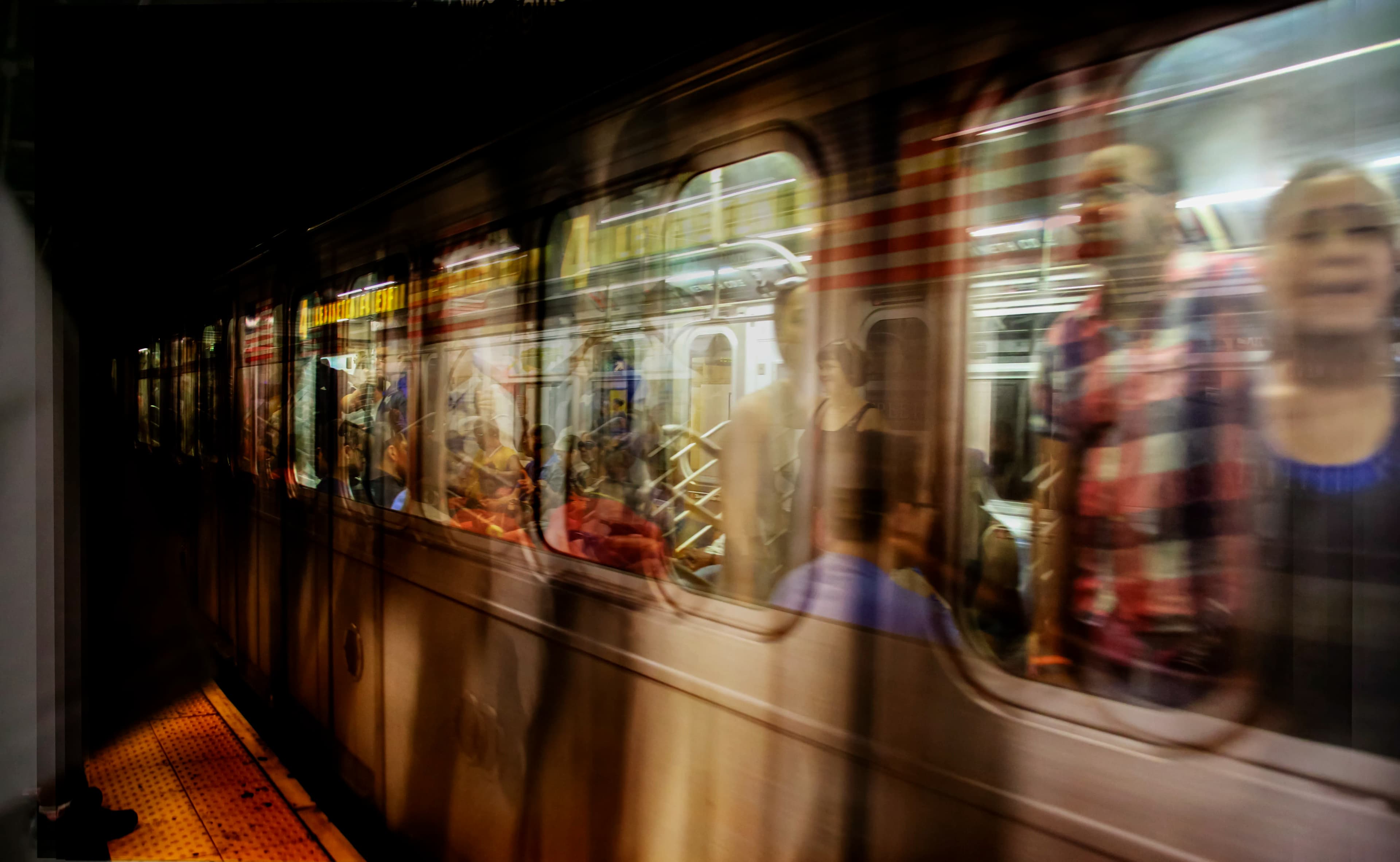 Moving New York City subway train photographed at 86th Street in Manhattan with passengers visible through blurred windows, created from multiple exposures and titled Passengers in Passing by Francisco Colón.
