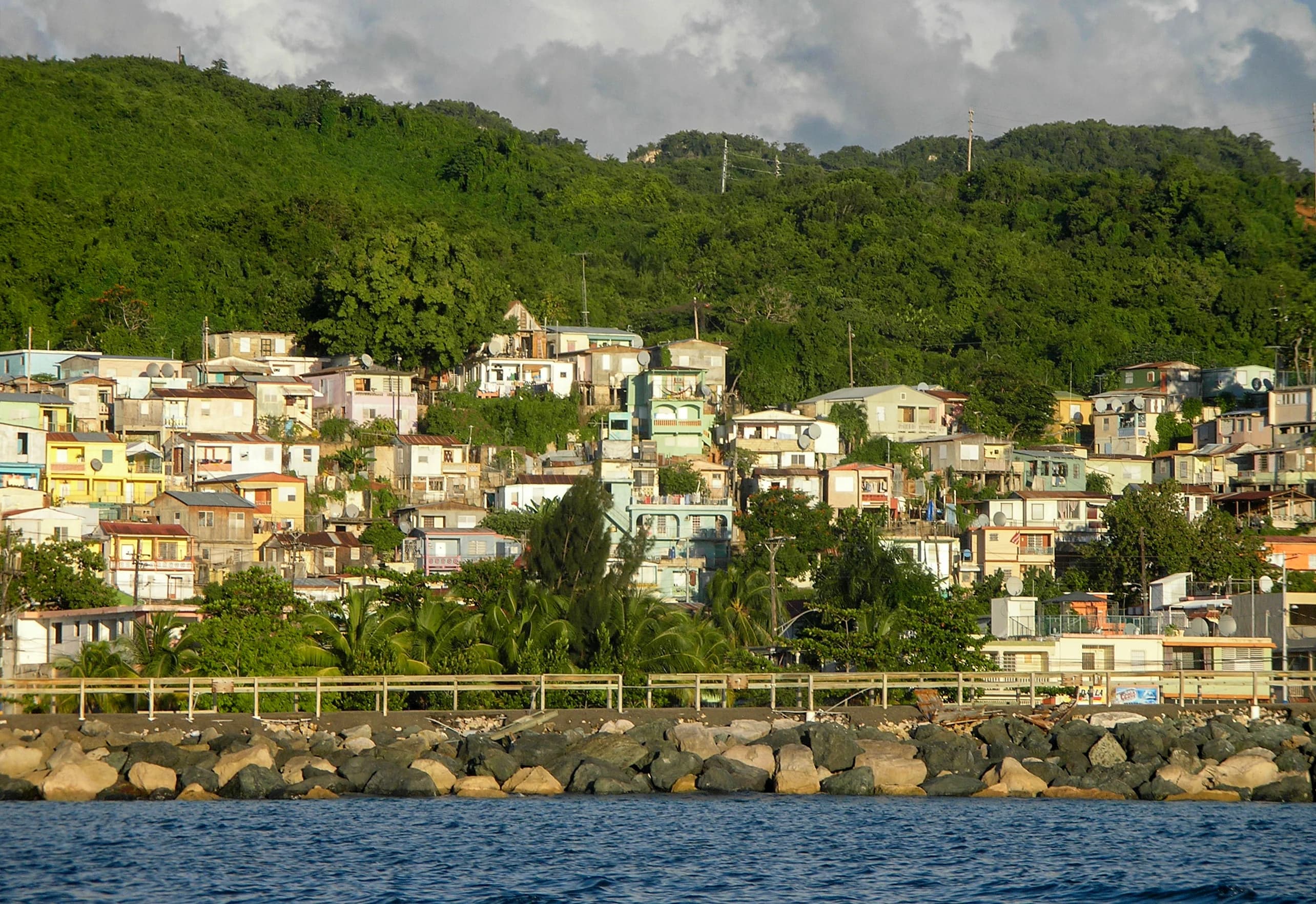 Hillside homes rising above the shoreline and blue water in Aguadilla, Puerto Rico.