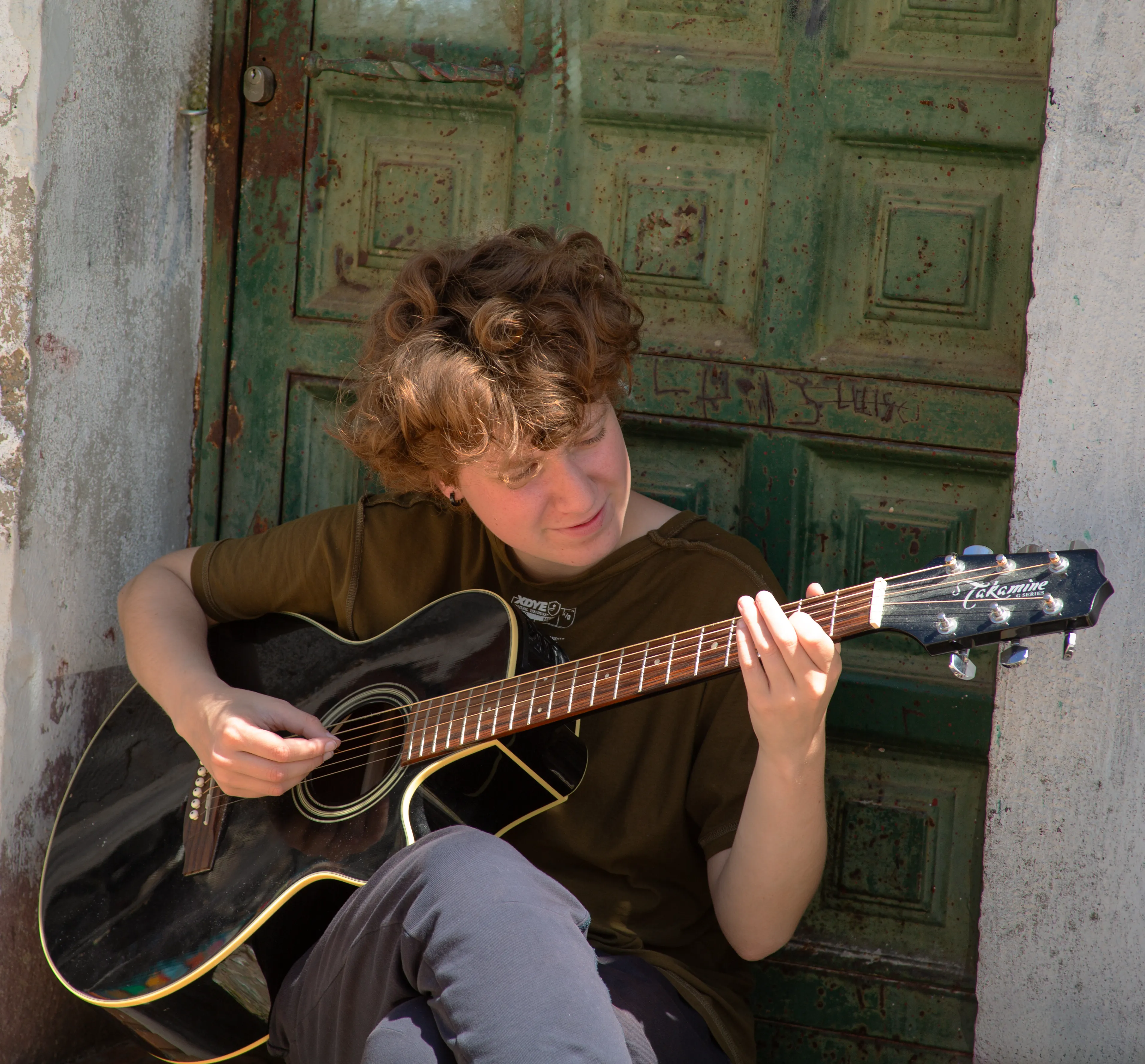 Young guitarist practicing beside a weathered doorway in Granada, Spain, titled The First Chord by Francisco Colón.