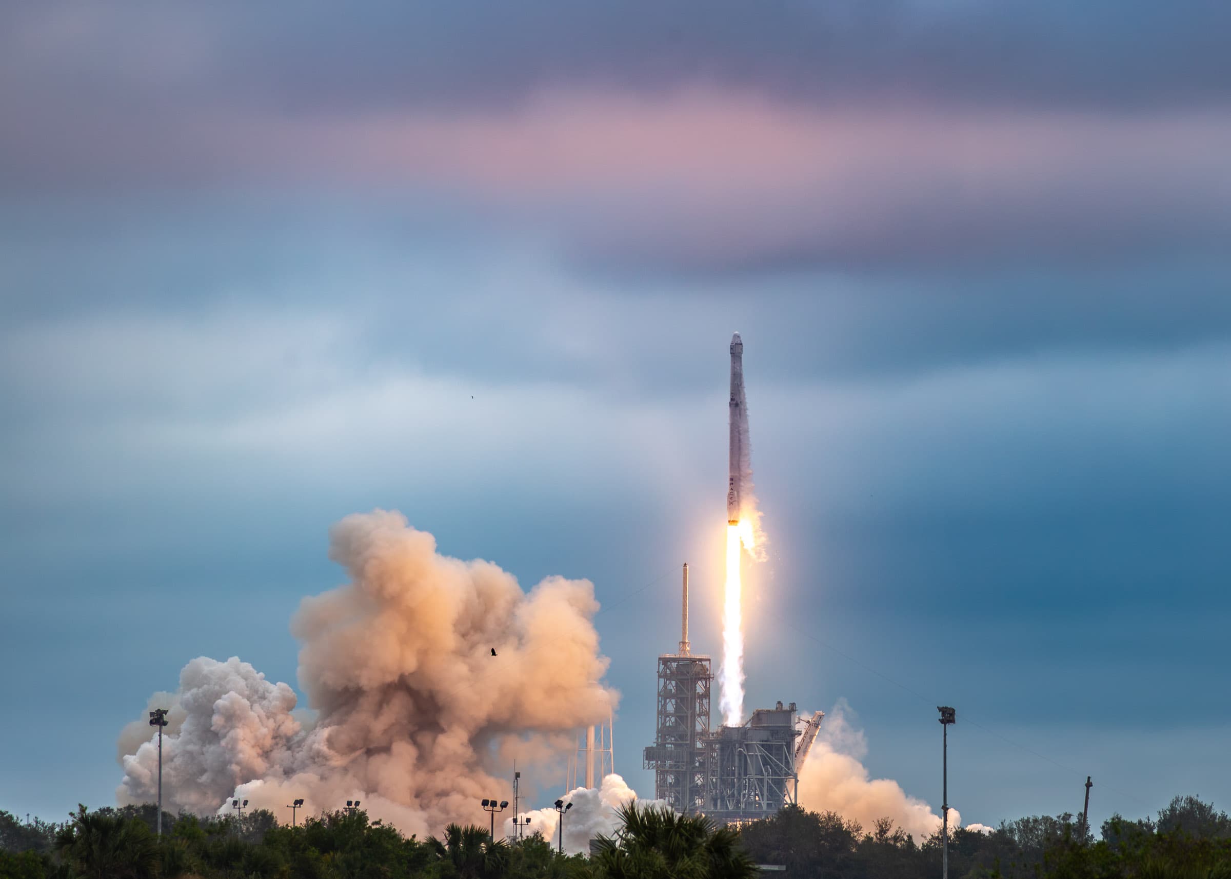SpaceX Falcon 9 rocket lifting off from Launch Complex 39A at Kennedy Space Center during the CRS-10 mission, with bright exhaust and expanding smoke beneath a blue-gray sky, photographed by Francisco Colón.