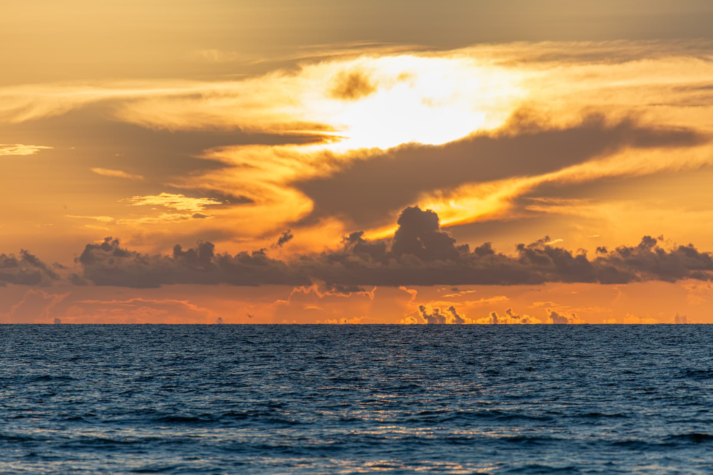 Deep blue Atlantic Ocean beneath an intense gold and orange sunrise with layered clouds over Miami Beach, photographed by Francisco Colón.