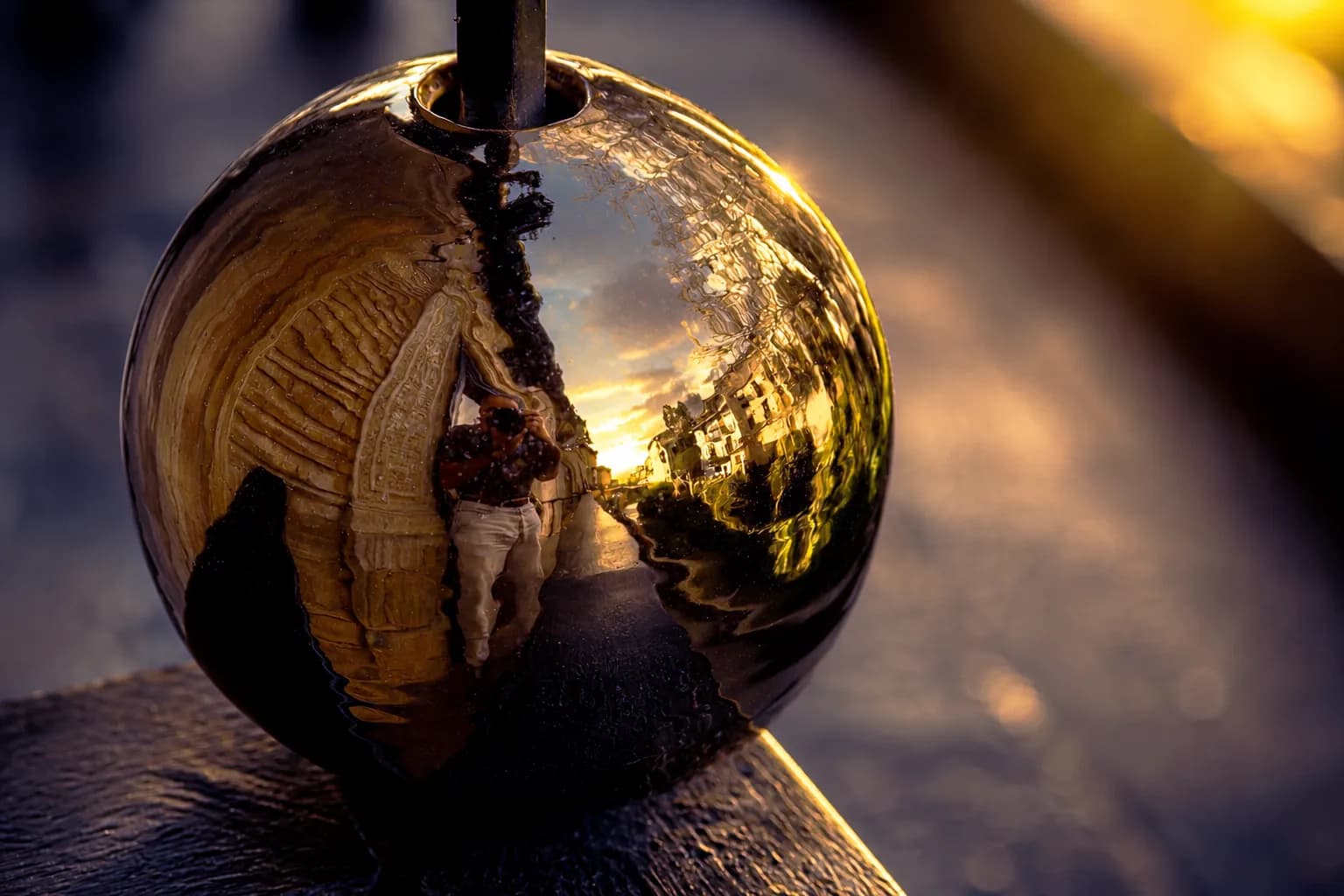 Photographer reflected with the city and evening sky in a polished metal sphere on a hotel balcony in Granada, titled The Photographer's Reflection by Francisco Colón.